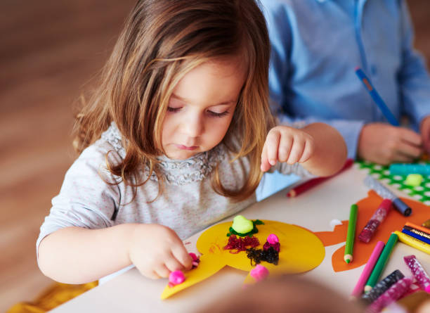 A young girl engaged in a creative craft activity, using colorful clay and pencils at a table. Ideal for early childhood education and sensory play.